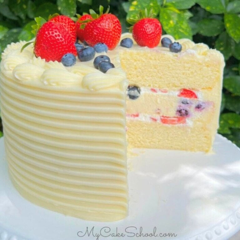 Sliced berry cheesecake cake on a cake pedestal, topped with fresh strawberries and blueberries.