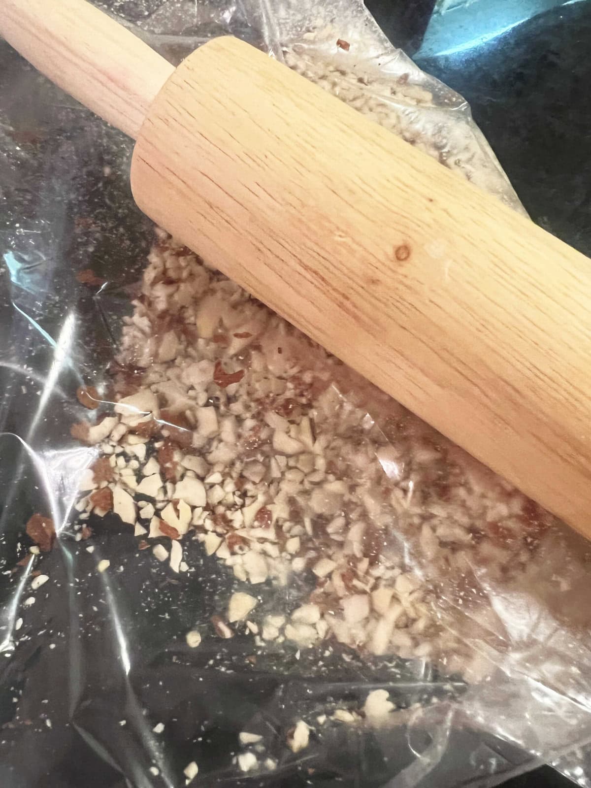 Crushing sliced almonds that are sealed in a ziplock bag, using a rolling pin.