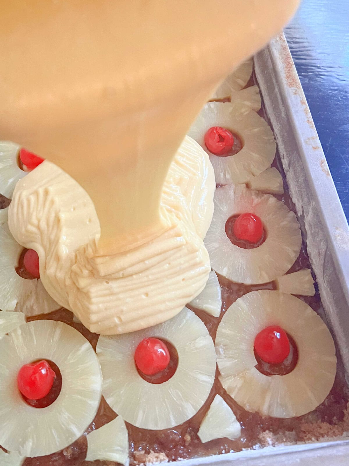 Pouring the cake batter over the pineapple rings and cherries.