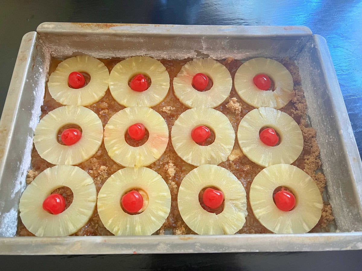 Pineapple rings and cherries on top of brown sugar in sheet cake pan.