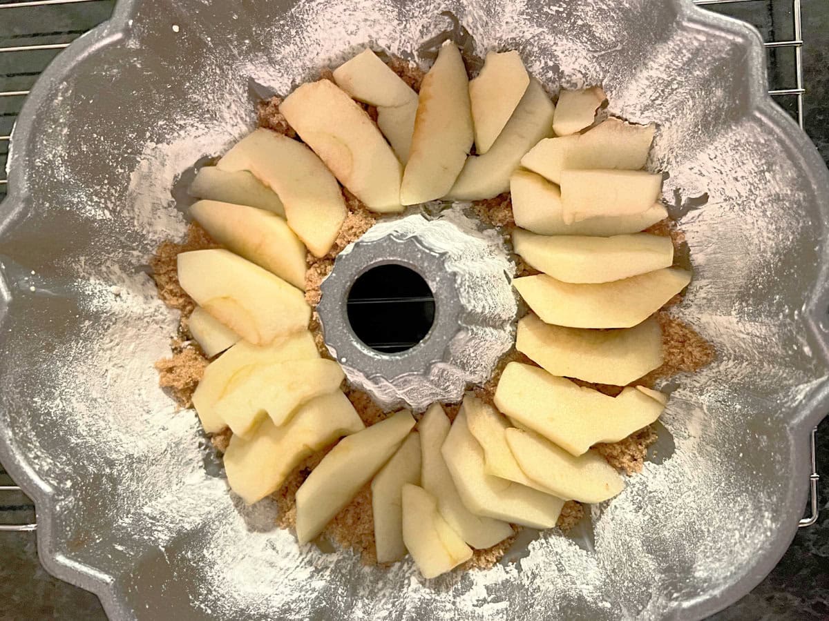 Apple slices arranged on top of the butter and sugar at the bottom of a prepared bundt pan.