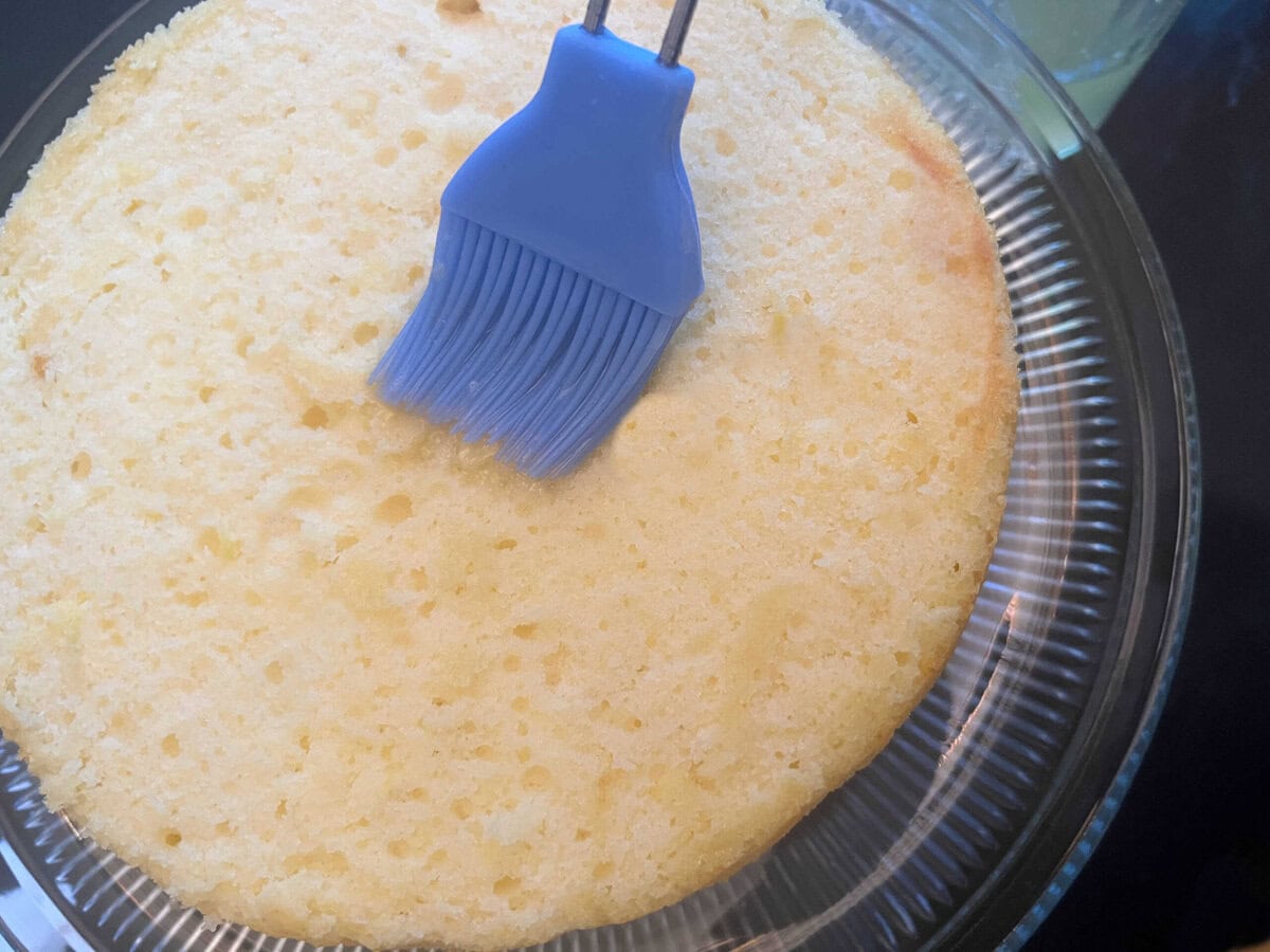 Brushing lemonade cake layer with lemonade, using a pastry brush.