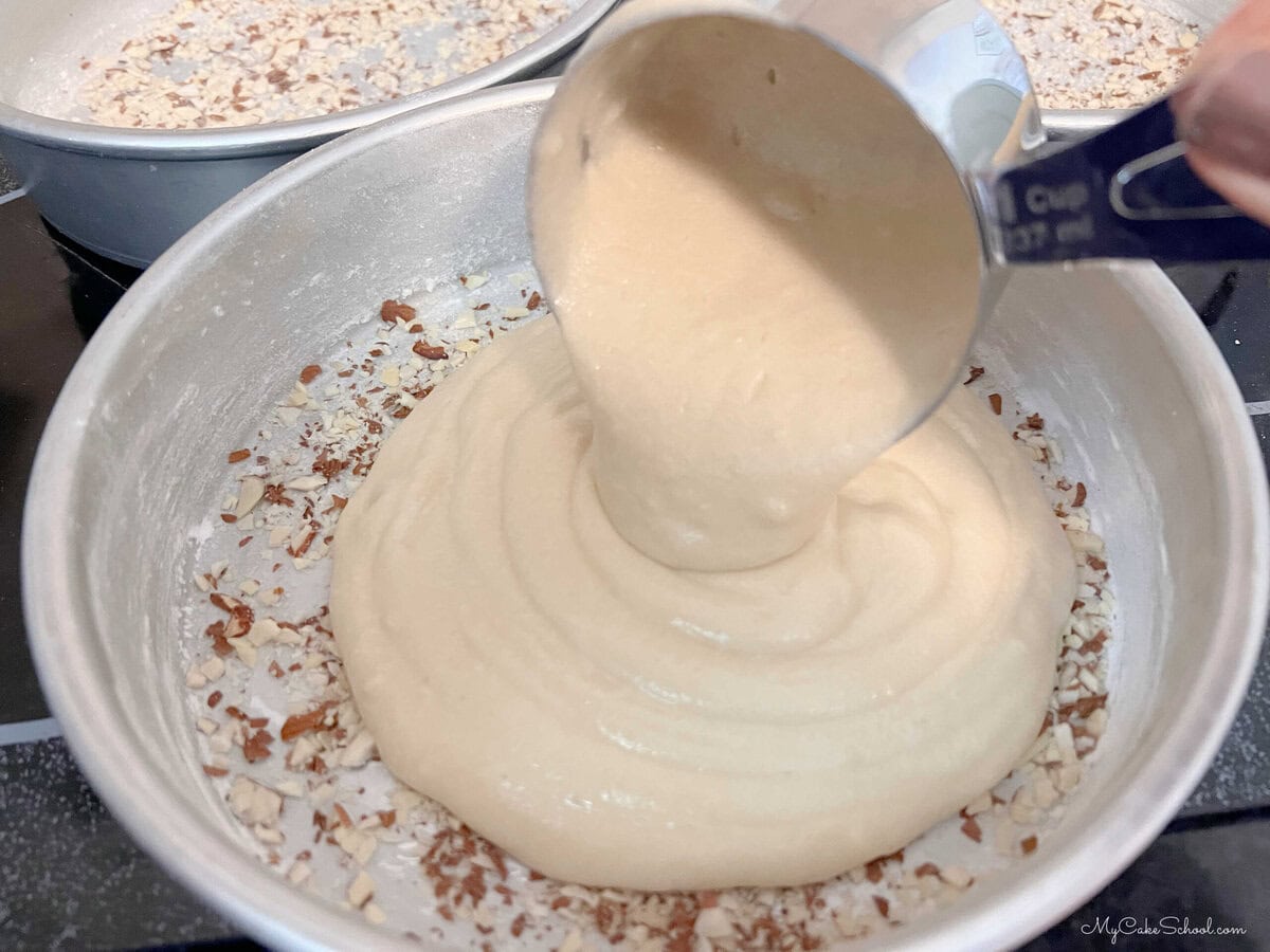 Pouring cake batter over the chopped almonds in each prepared 8 inch pan.