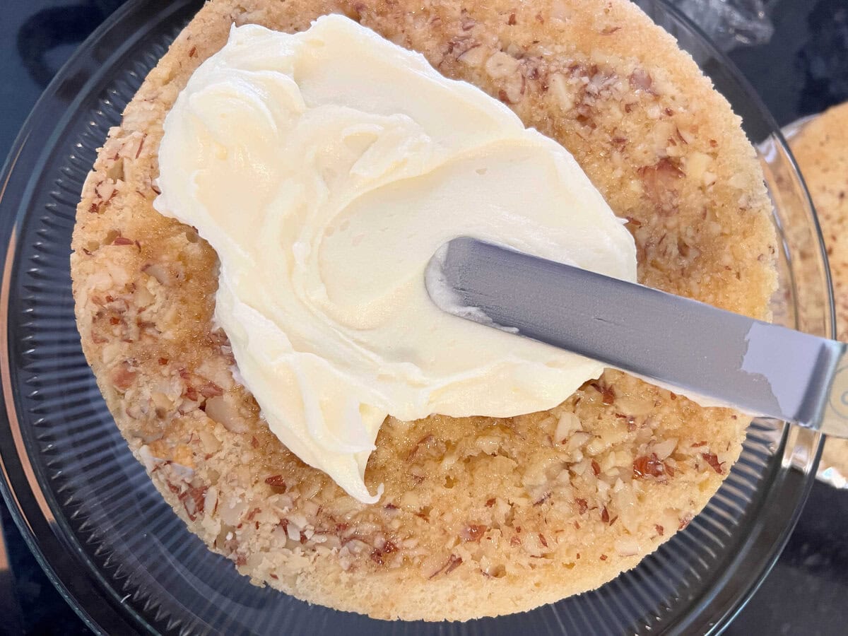 Spreading almond cream cheese frosting over the glazed cake layer.