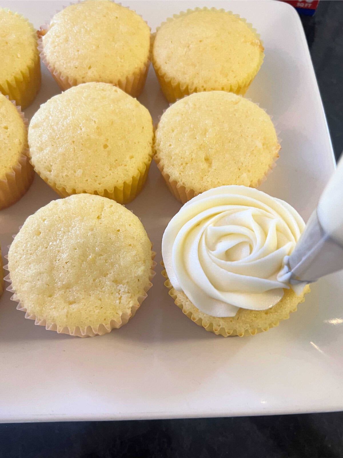 Piping swirls of frosting onto the cooled cupcakes.