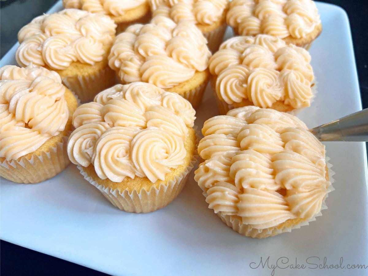 Piping shells and stars onto the orange cupcakes with orange cream cheese frosting.