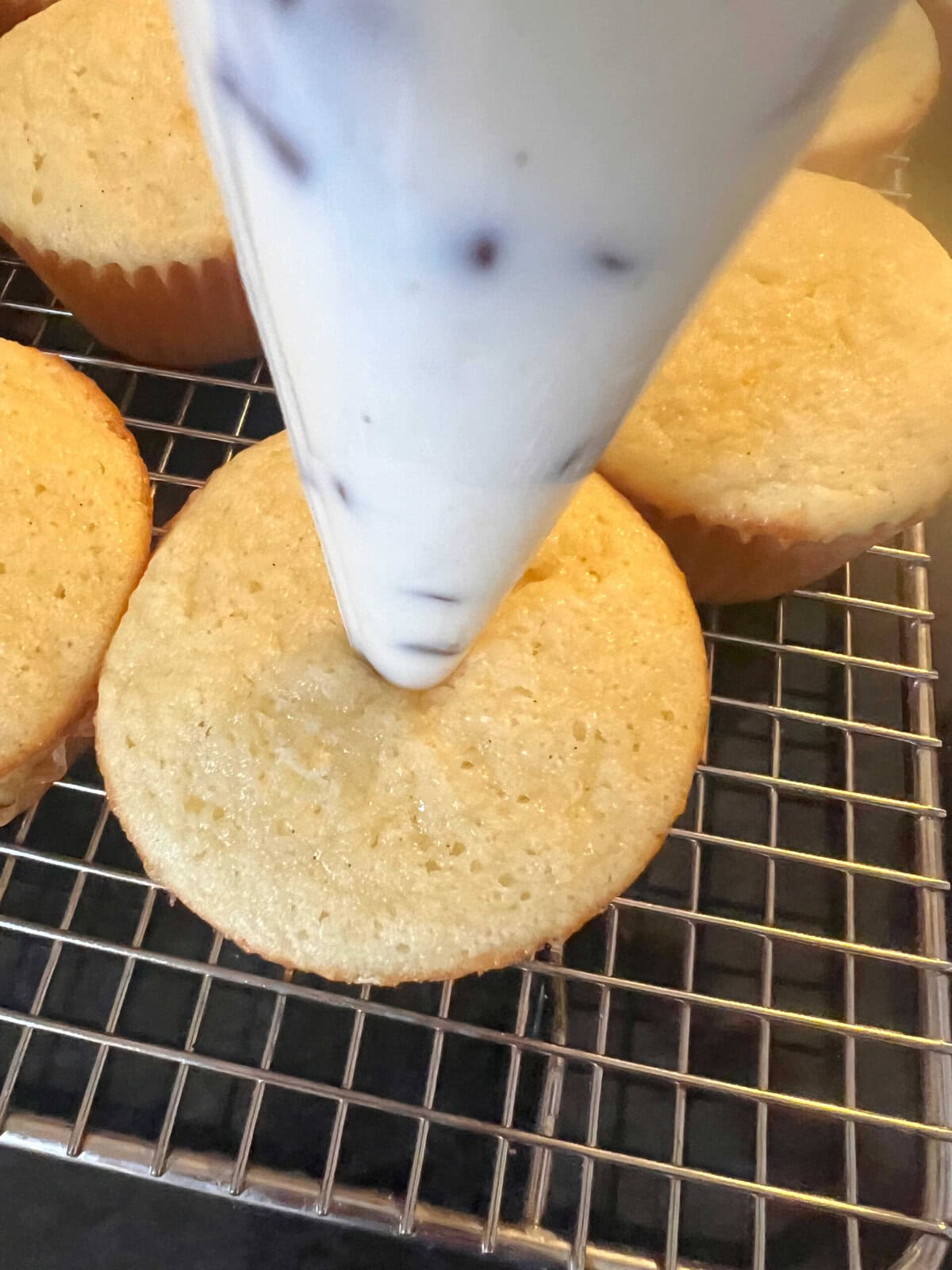 Piping bag of mascarpone chocolate chip filling inserted into the top of a cupcake.