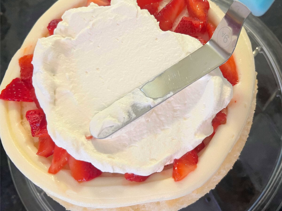 Spreading whipped cream over the sliced strawberries.